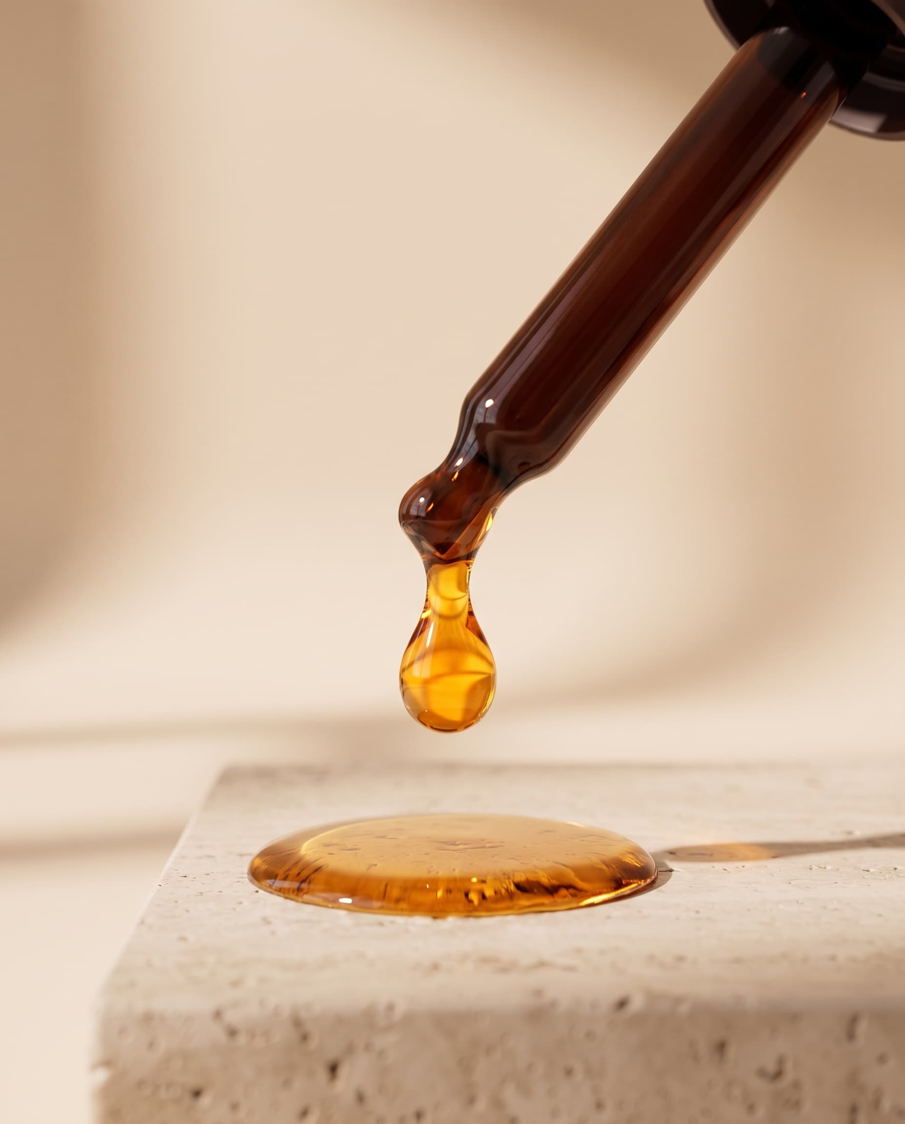 A glossy amber drop of batana oil falling from the dropper