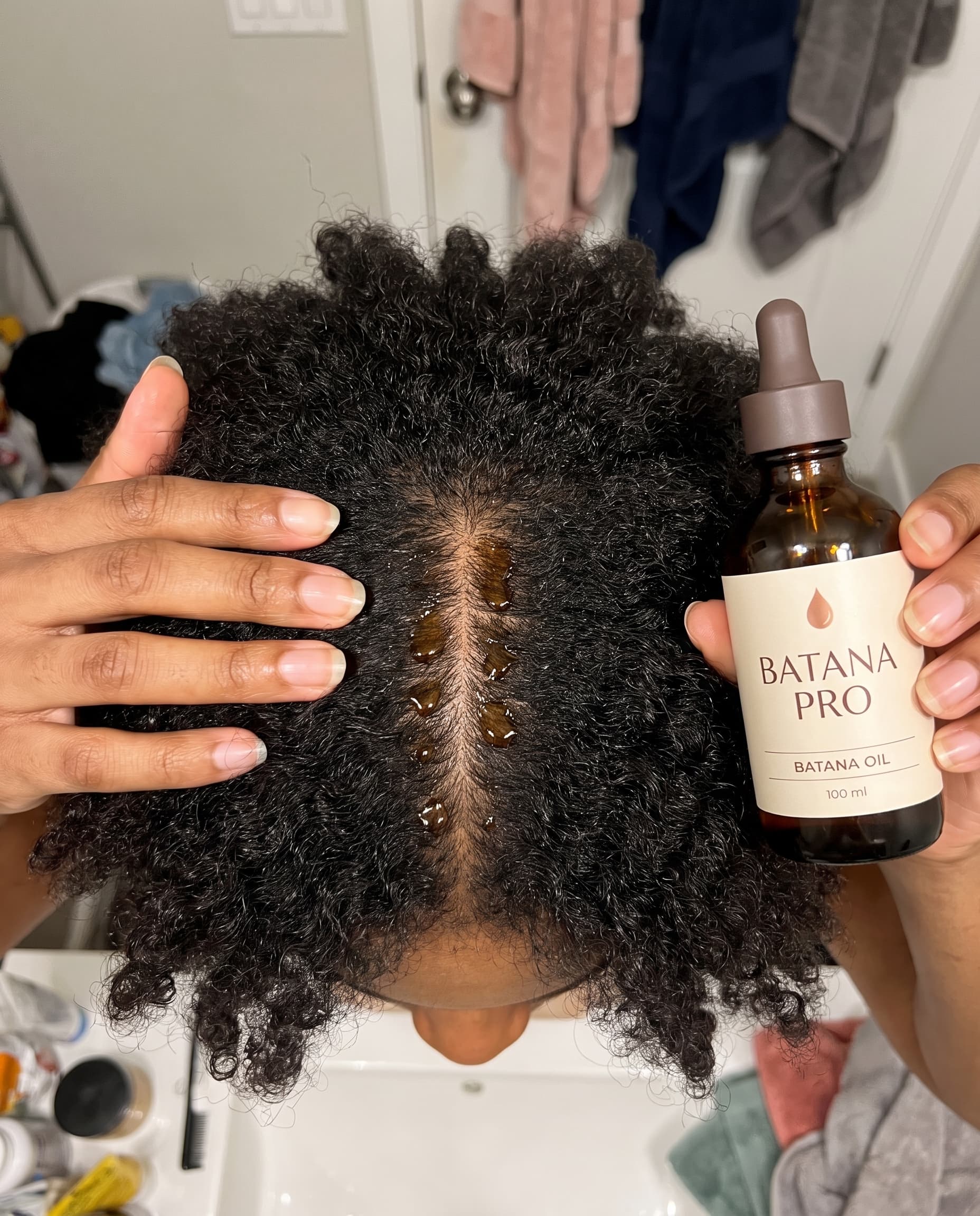 Drops of batana oil along a centre parting in thick coily hair